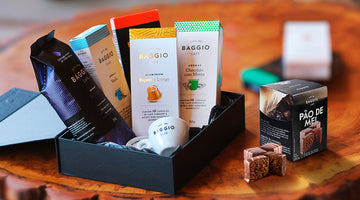 Pacotes de café Baggio dispostos em uma caixa de presentes junto com uma xícara e um pão de mel ao lado.
