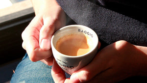 Pessoa com uma xícara de café Baggio nas mãos, enquanto uma fumaça sobe do líquido, indicando que ele está quente.