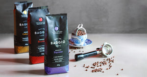 Três tipos de cafés Baggio em uma mesa com alguns grãos espalhados e uma xícara ao fundo.