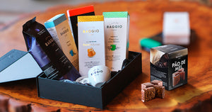 Pacotes de café Baggio dispostos em uma caixa de presentes junto com uma xícara e um pão de mel ao lado.