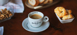 Xícara de cappuccino Baggio em uma mesa de madeira com alguns pães ao redor.